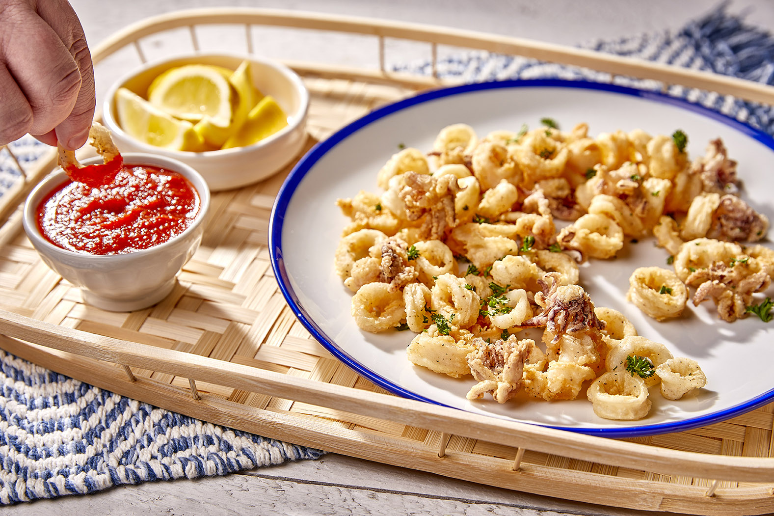 Fried Calamari on a blue-rimmed white plate with bowls of marinara and lemon wedges.