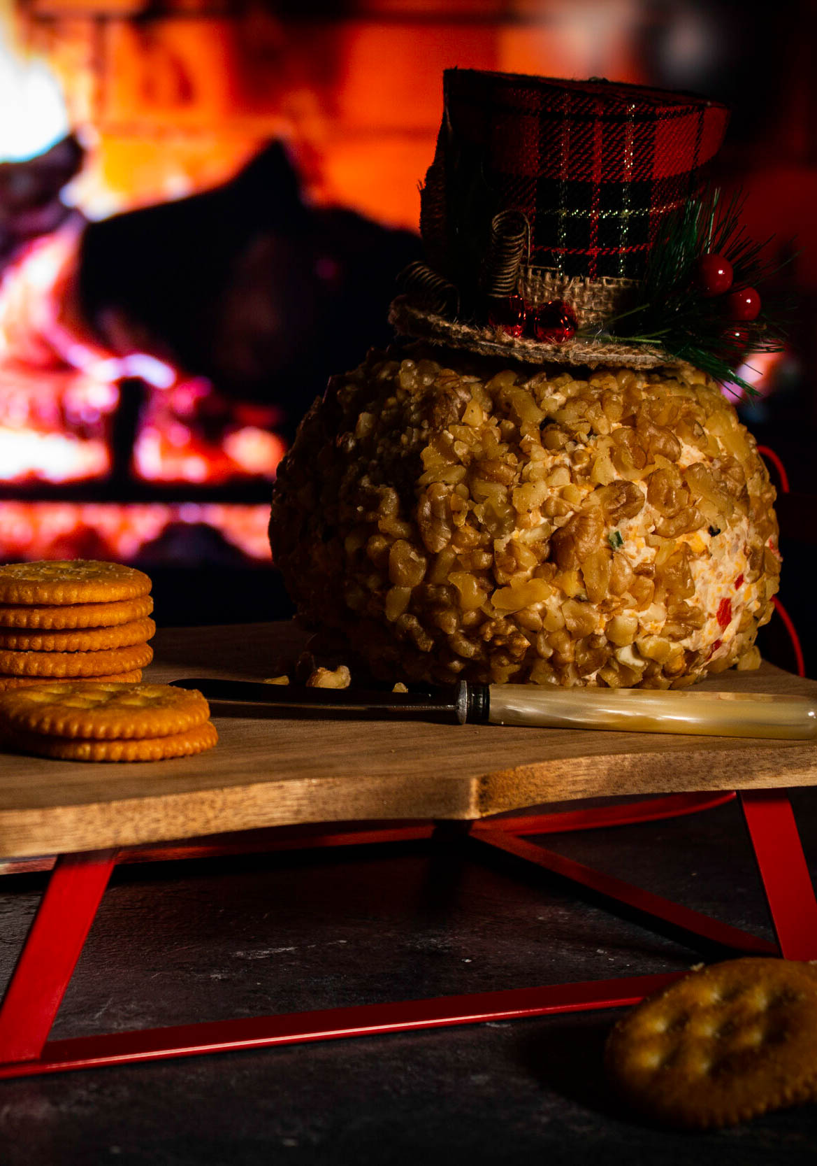Cheeseball wearing a top hat on a sleigh cutting board with butter crackers and a knife.