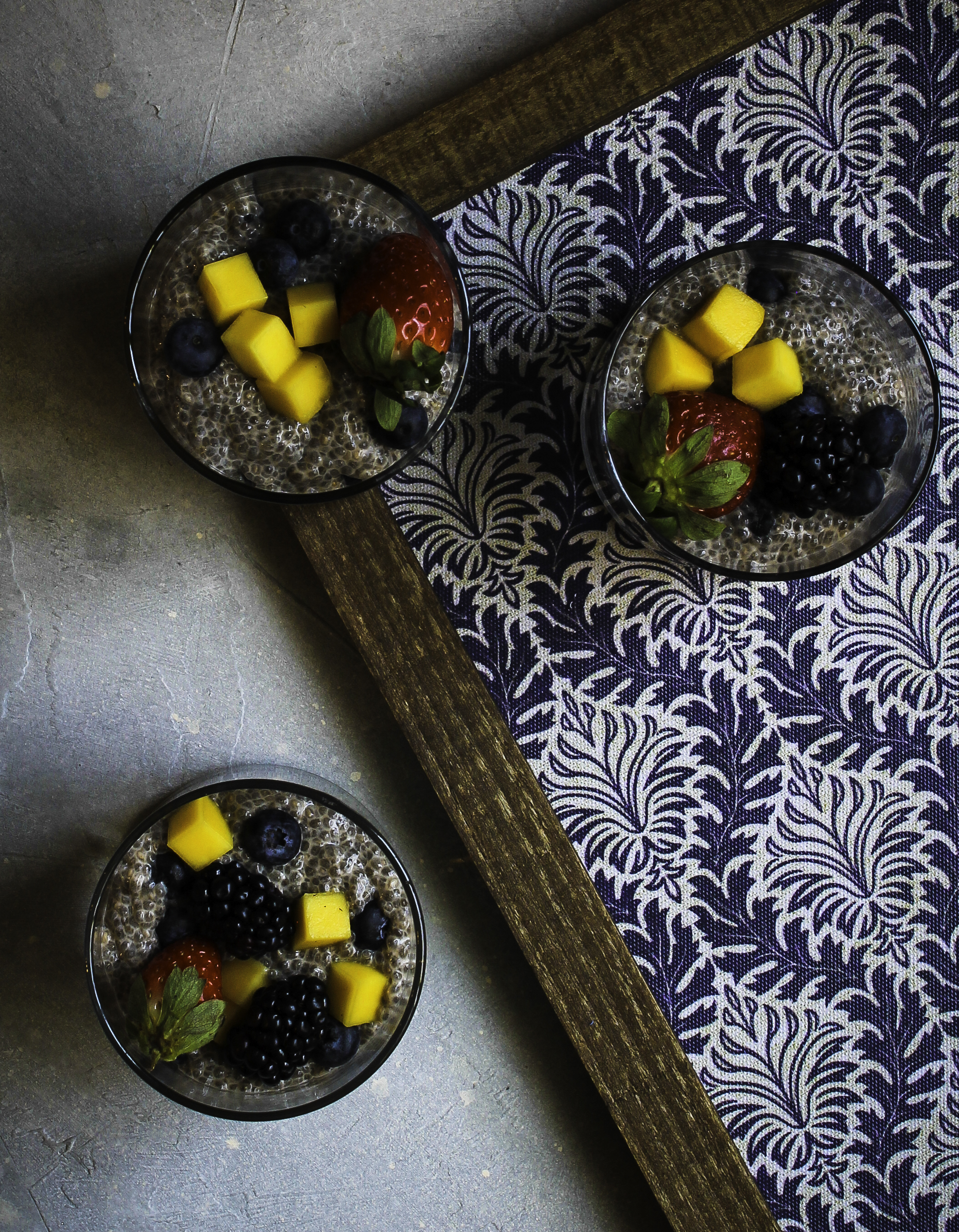 Chia pudding cups with mango, strawberry, blackberry and blueberry topping on a decorative blue and white patterned frame.