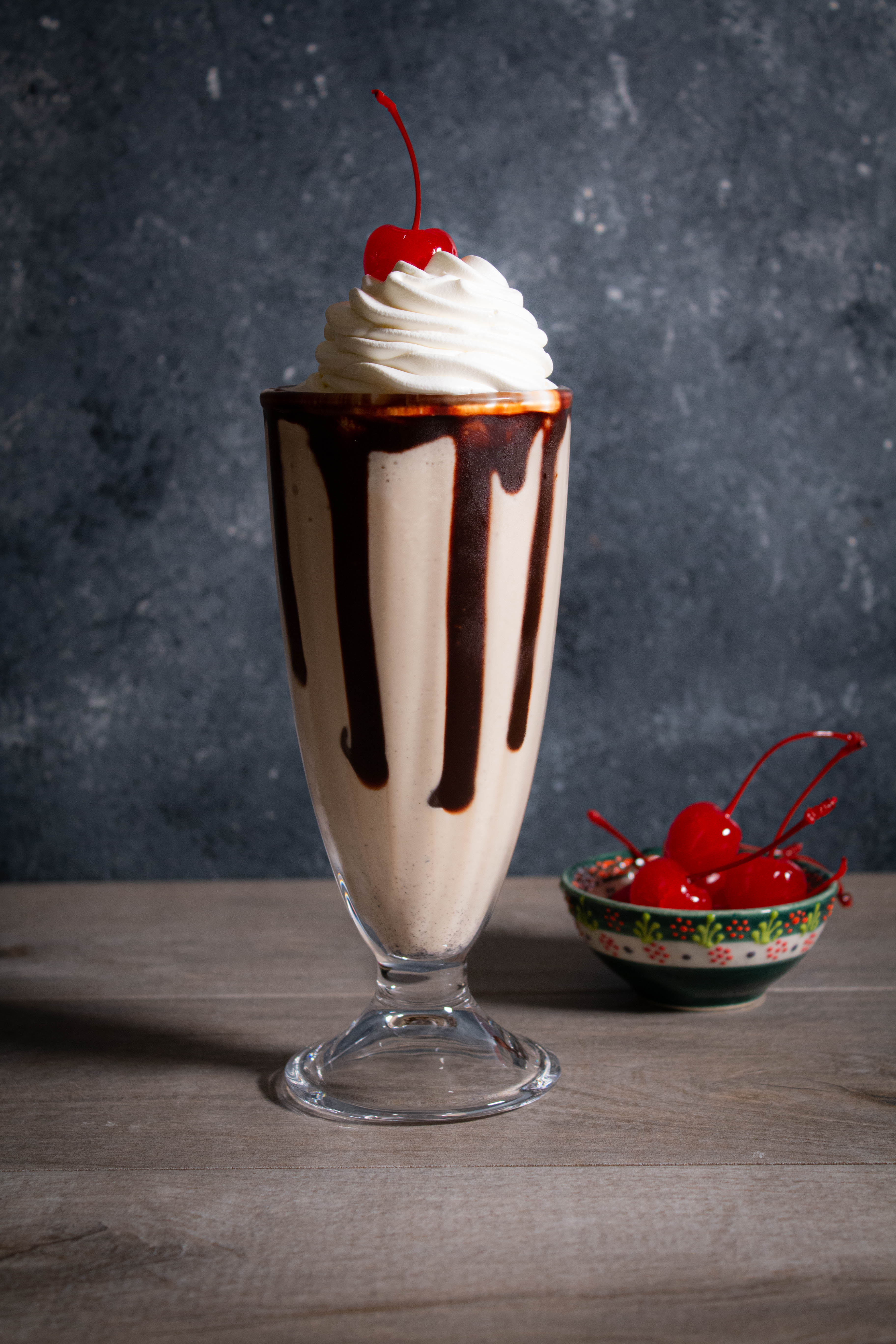 Frozen cold brew mudslide in a milkshake glass with chocolate drips, whipped cream and a cherry.