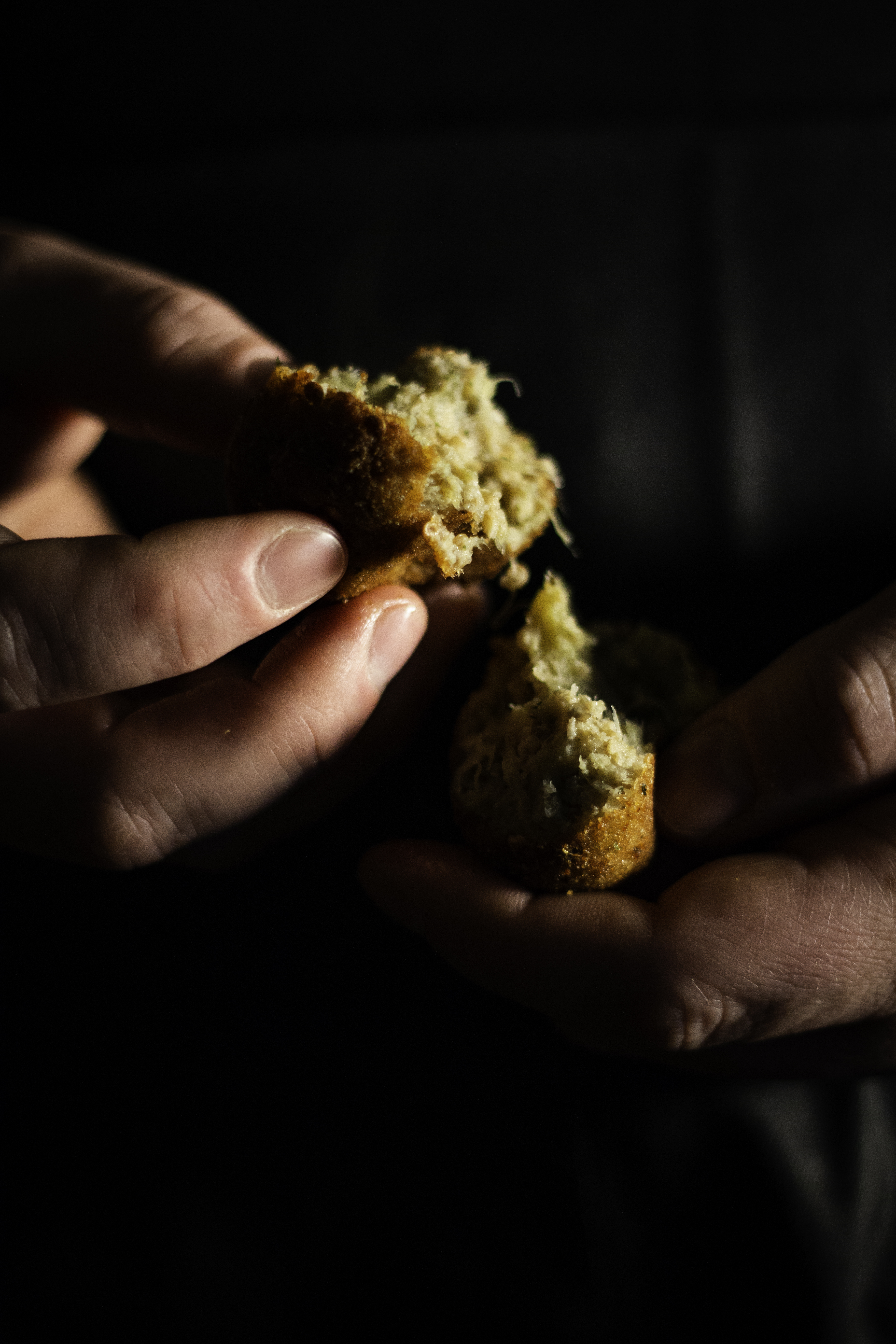 Hands tearing apart a freshly fried eggplant ball with a black background. 