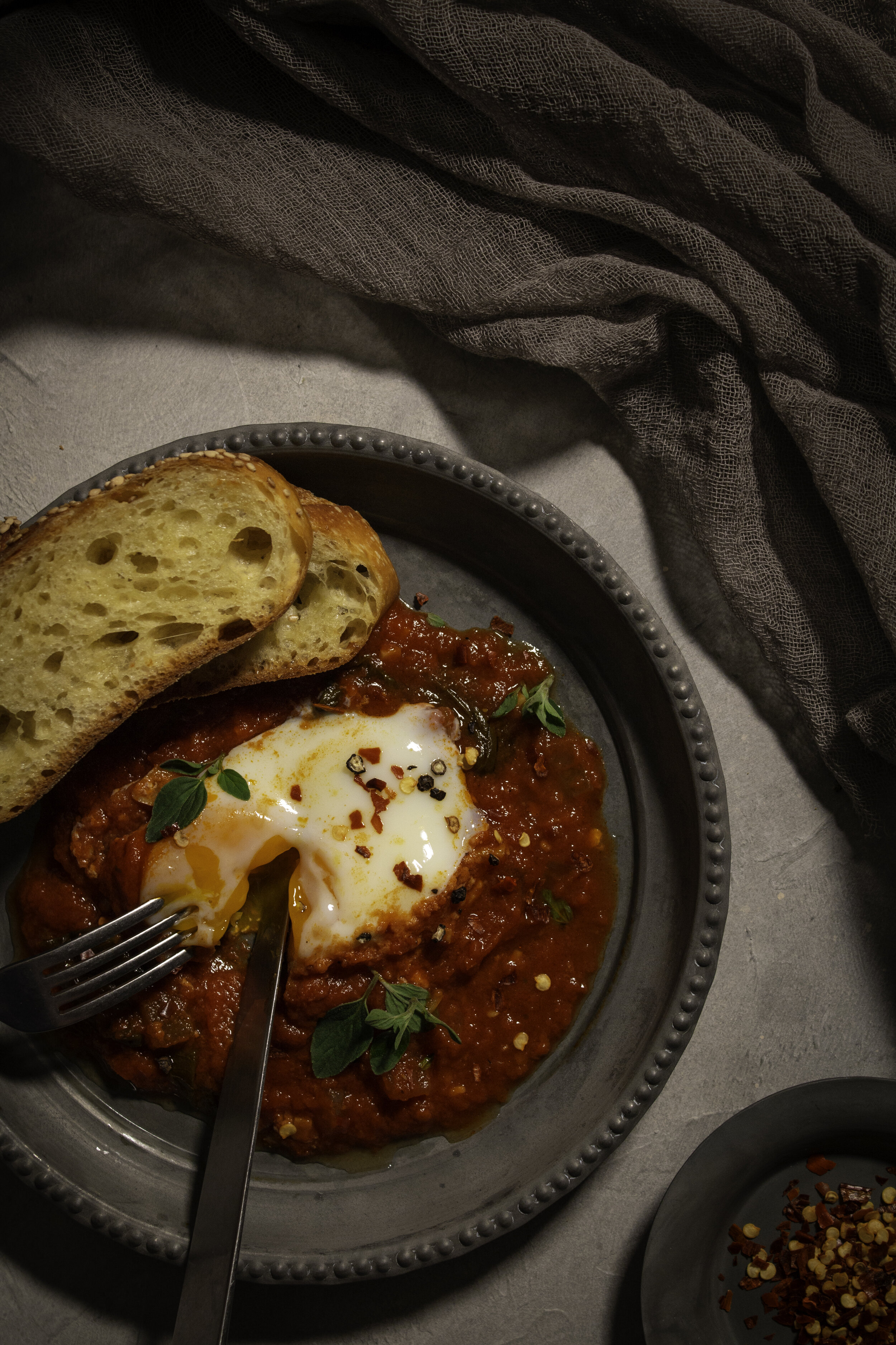 Soft cooked egg in tomato sauce with crostini on a grey plate.