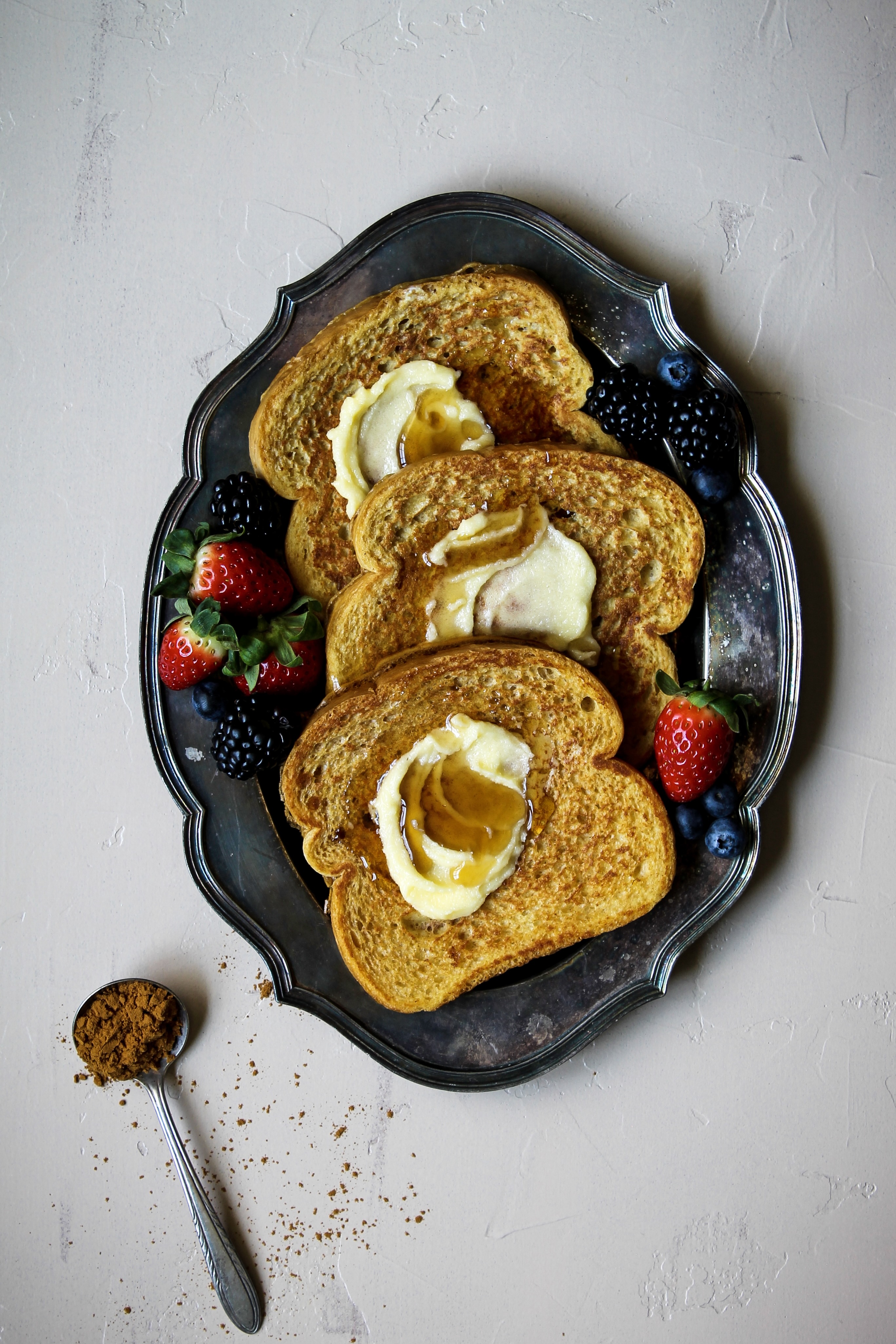Oval metal platter with 3 slices of French toast with butter, syrup and fresh berries.