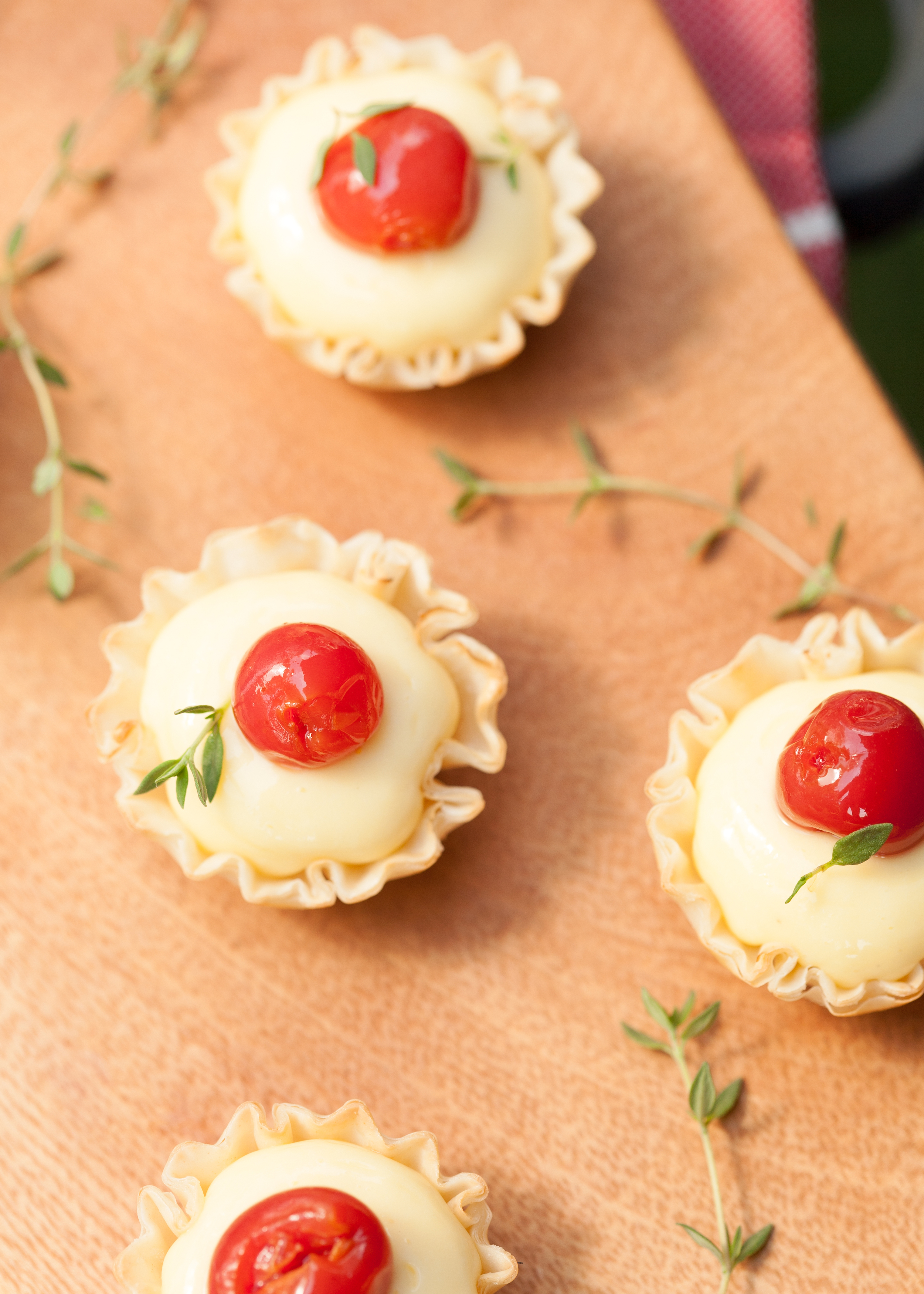 Mini lemon tarts with cherry and thyme garnish on a wooden board.