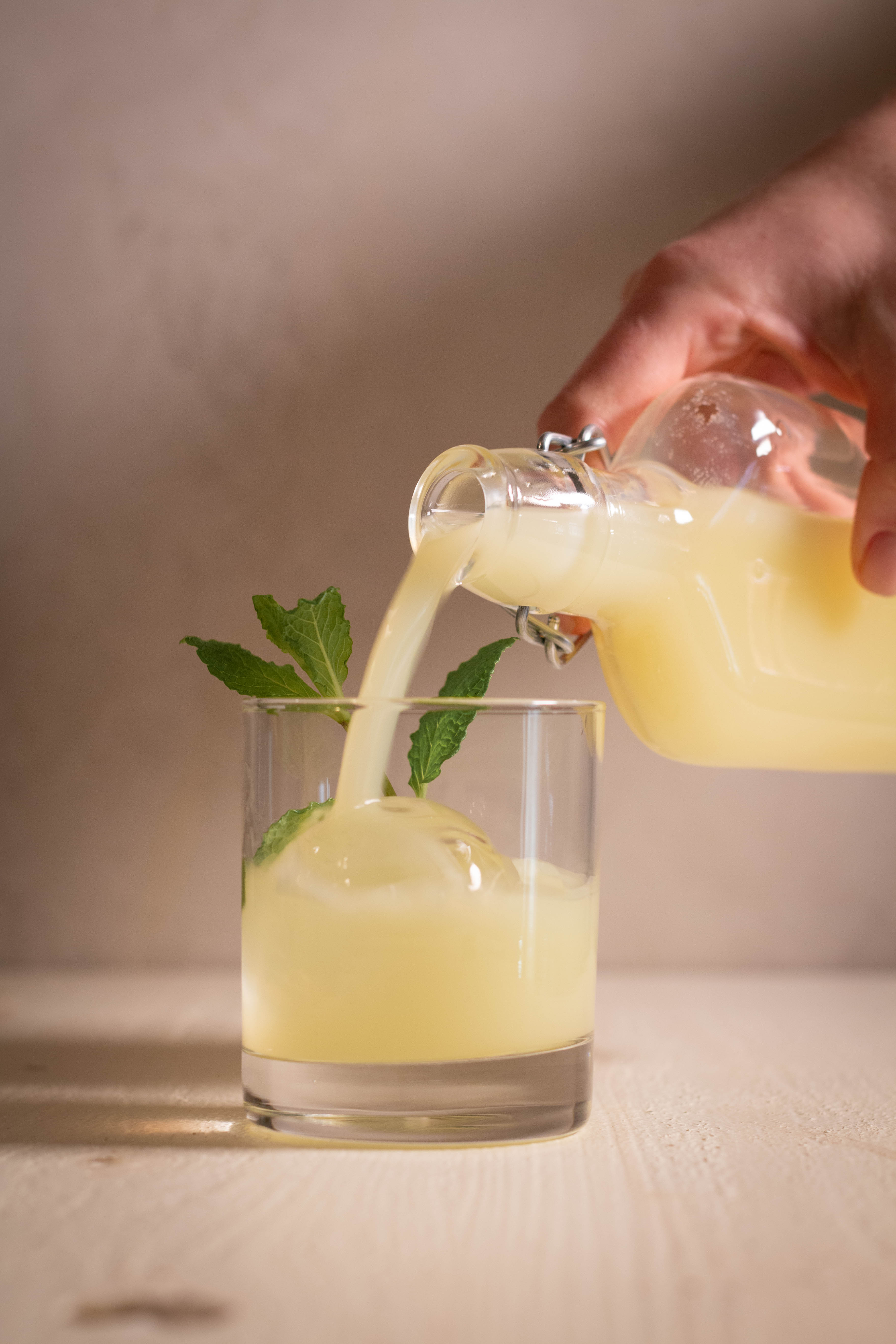 Limoncello being poured into a rocks glass with clear round cube and mint garnish.
