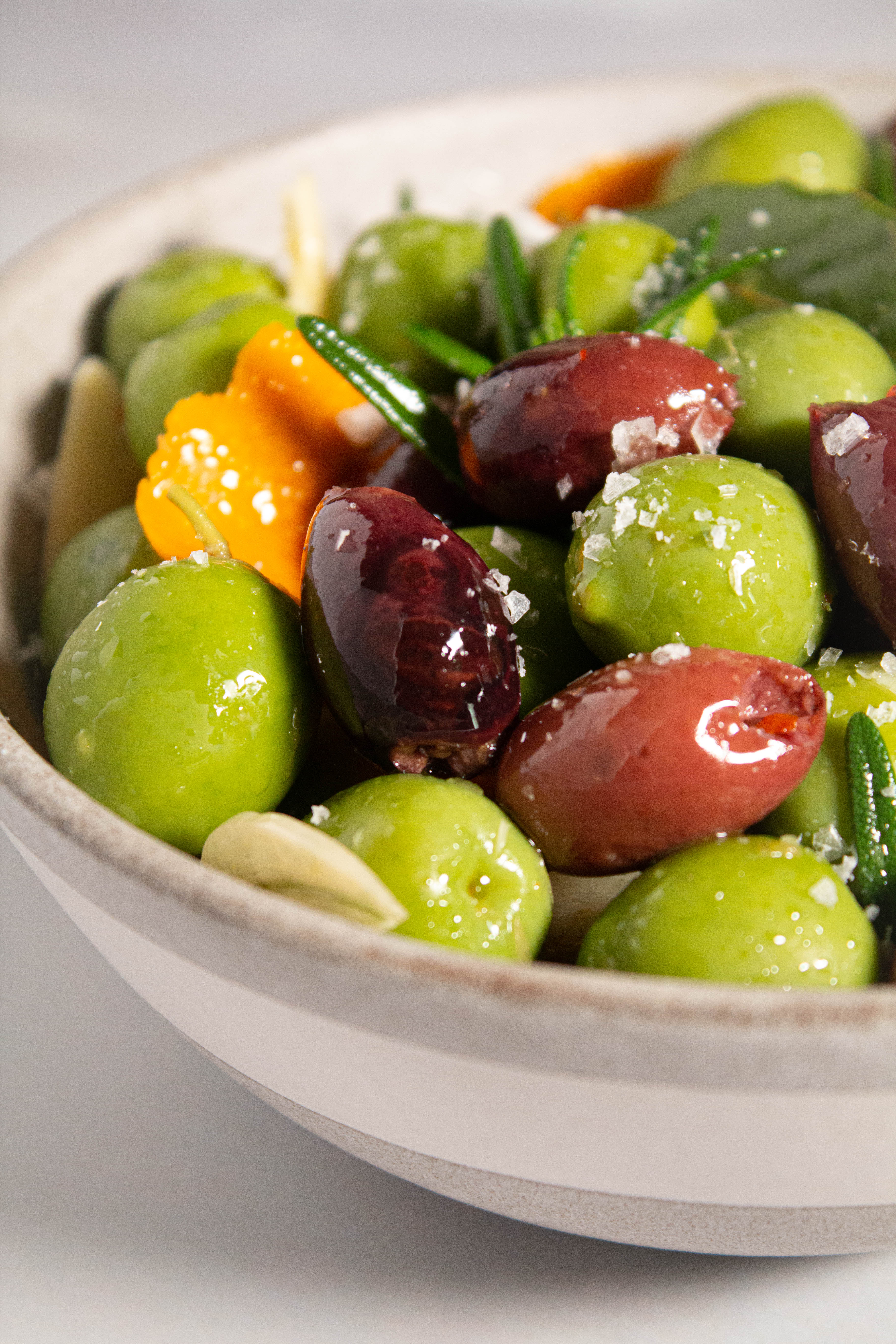 Gray bowl with marinated olives, orange peel, fresh rosemary and sliced garlic.