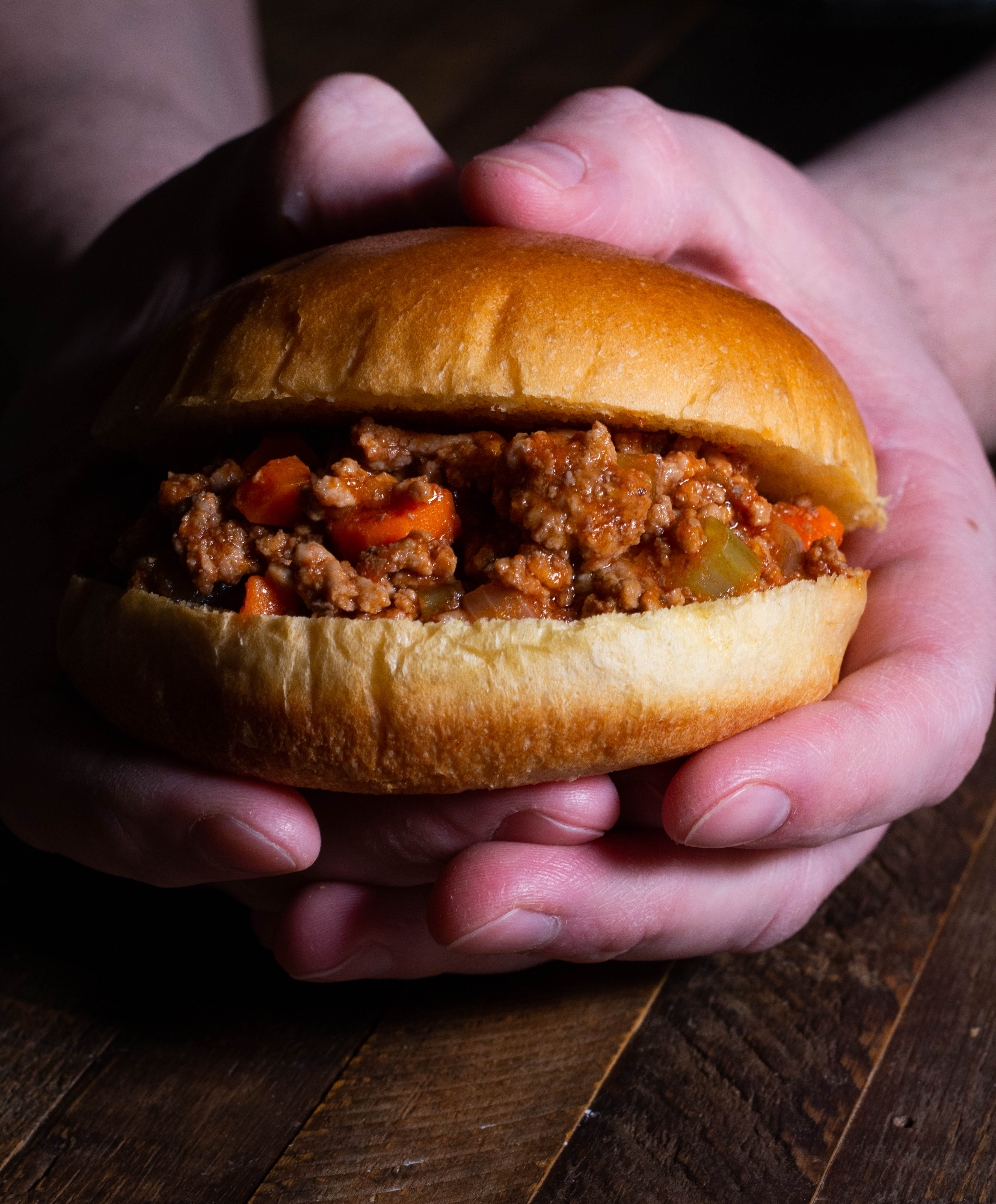 Pair of hands holding a brioche bun with bolognese.