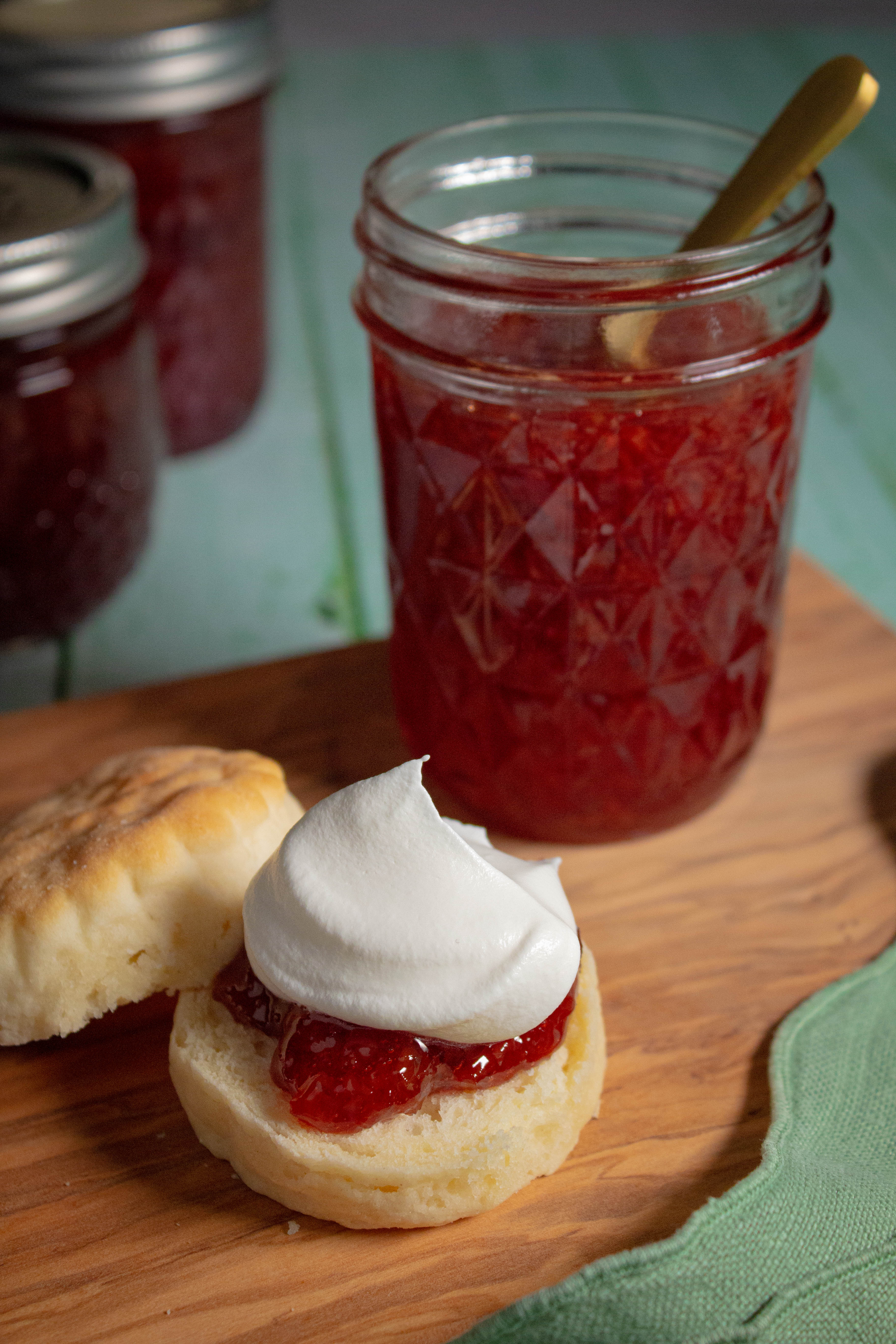 Biscuit topped with sour cherry jam and whipped cream with a mason jar with sour cherry jam in the background.