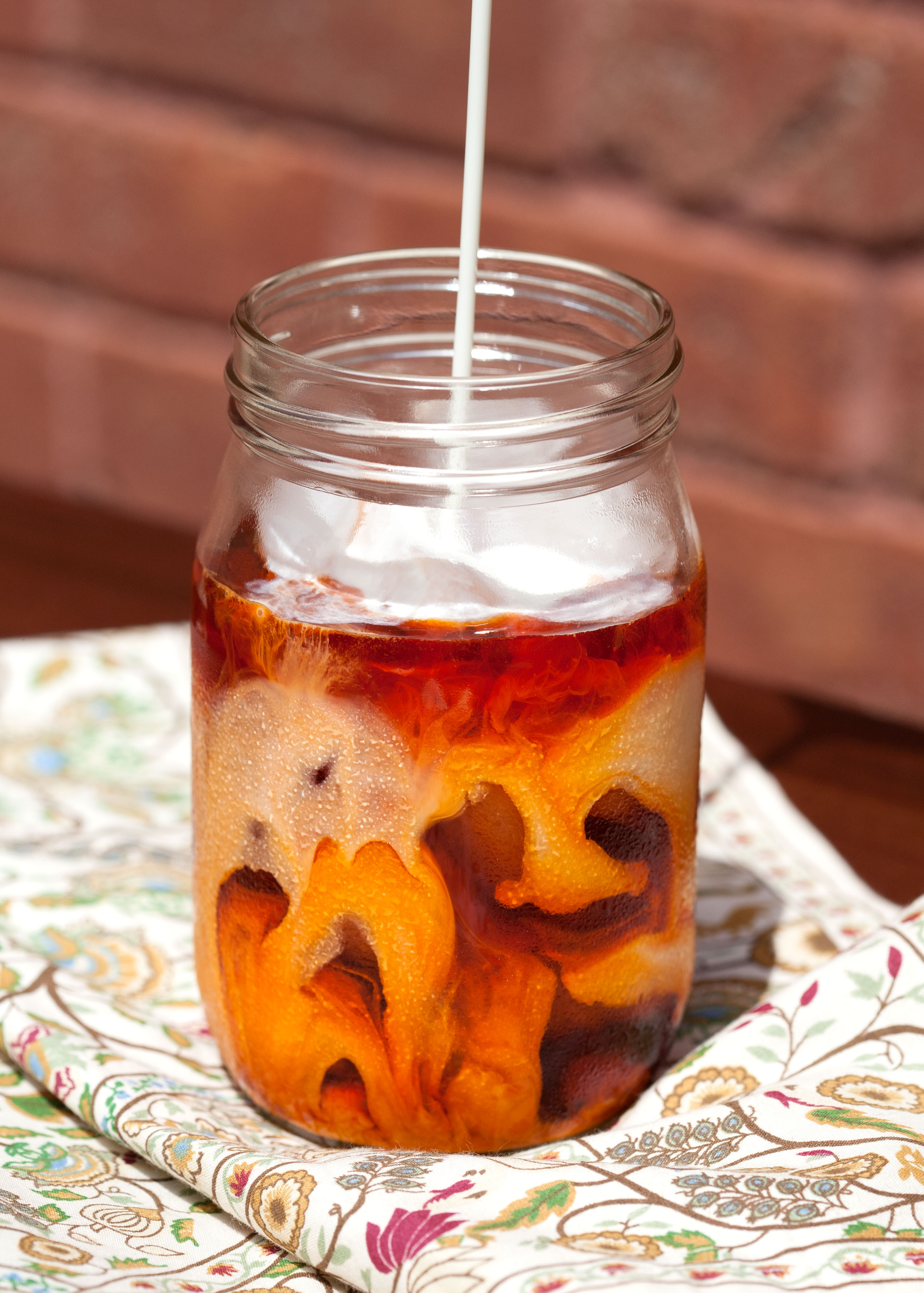 Mason jar with sweetened cream mixture pouring into tea mixture.