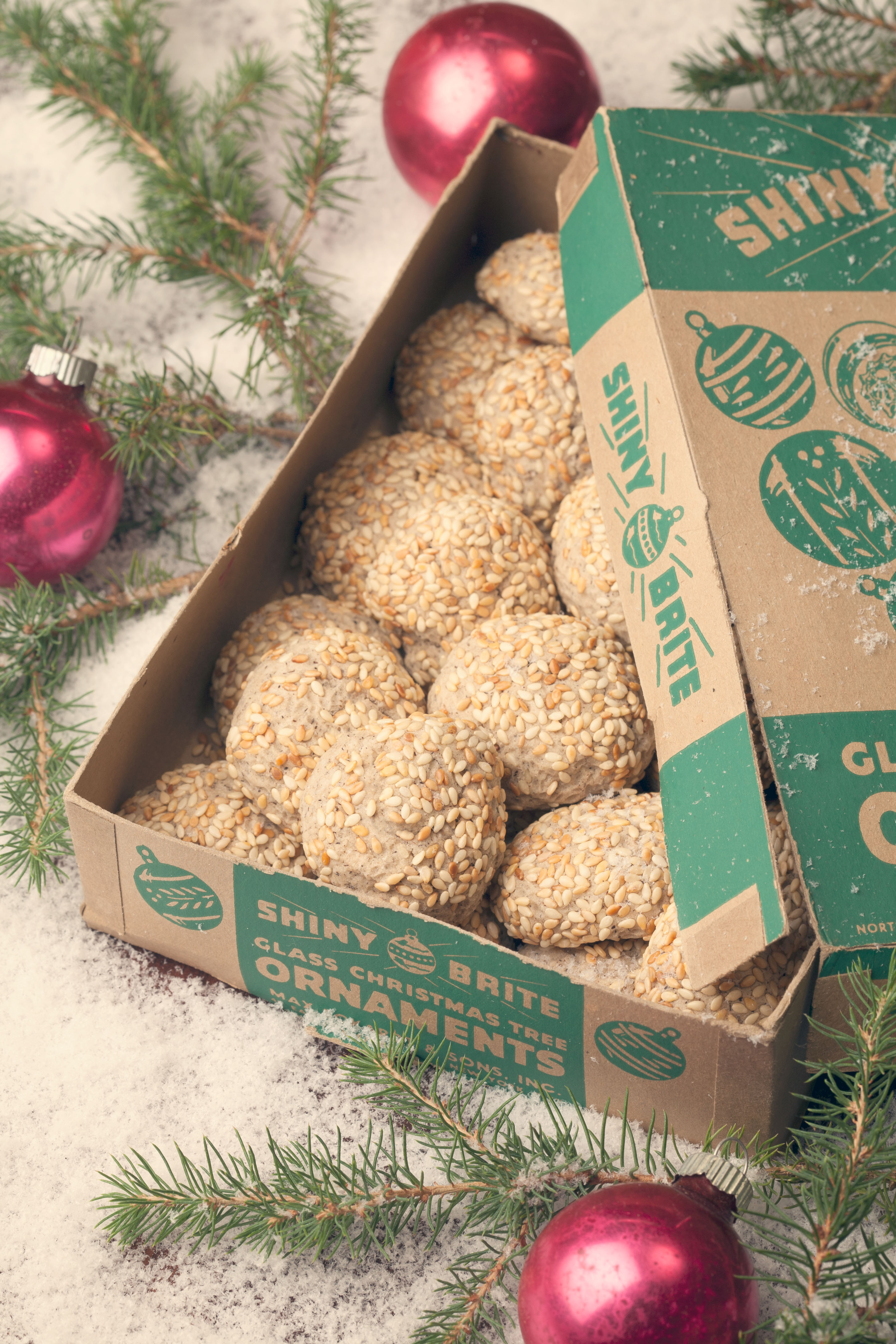 Toasted sesame cookies in a vintage ornament box surrounded by winter greens, ornaments and snow.