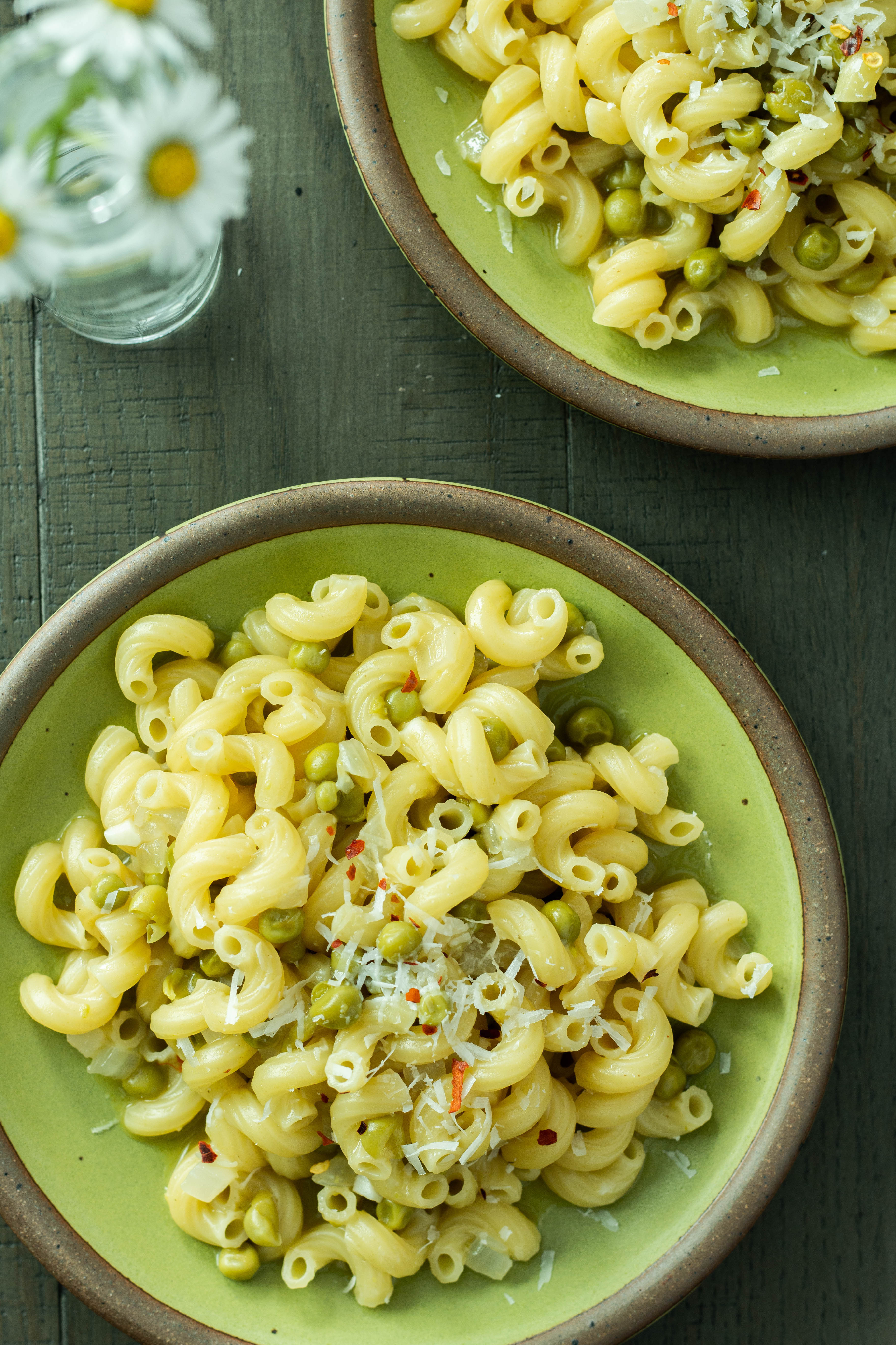 2 green plates with mounds of elbow macaroni and peas with grated cheese.